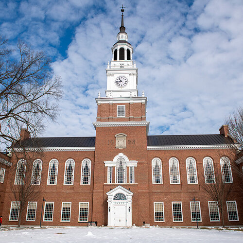 The exterior of a brick building with a large clock tower. Snow covers the ground in front of the building. 500x500