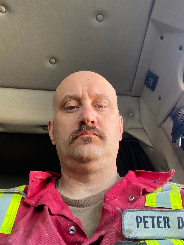 Peter Downing at work stating at the camera in a red uniform with neon vest and name tag